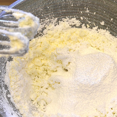 Adding powdered sugar to the creamed butter to make buttercream frosting.